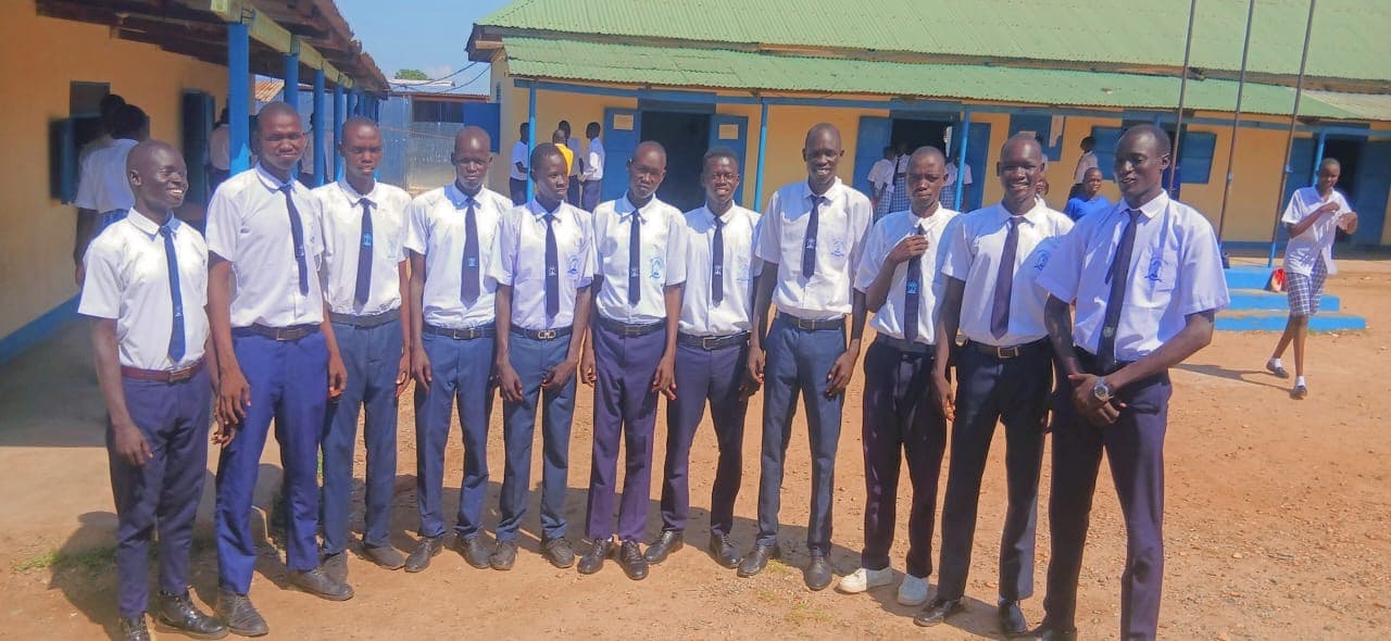 Students in school uniform standing in front of a classroom building at Gideon Seed Academy Secondary School