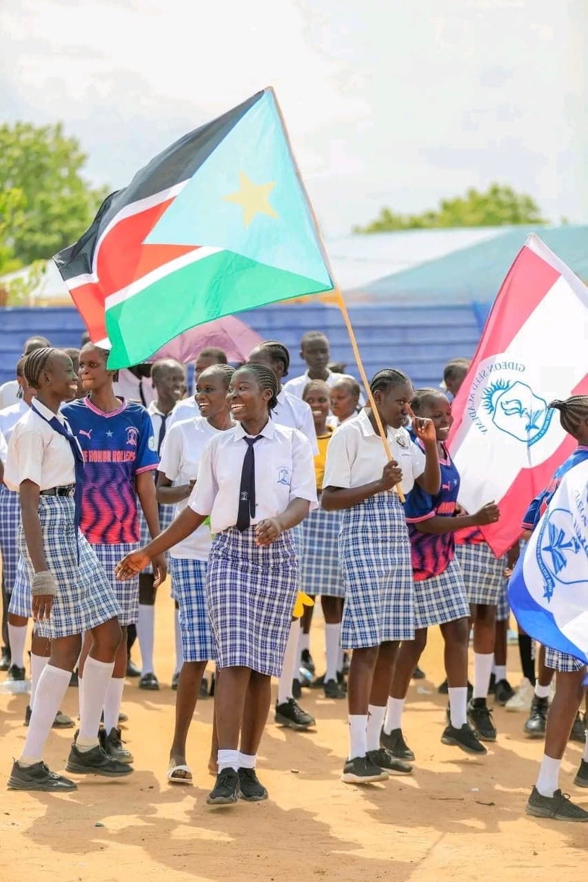 Students in school uniform carrying the South Sudan national flag and the Gideon Seed Academy school flag during a procession